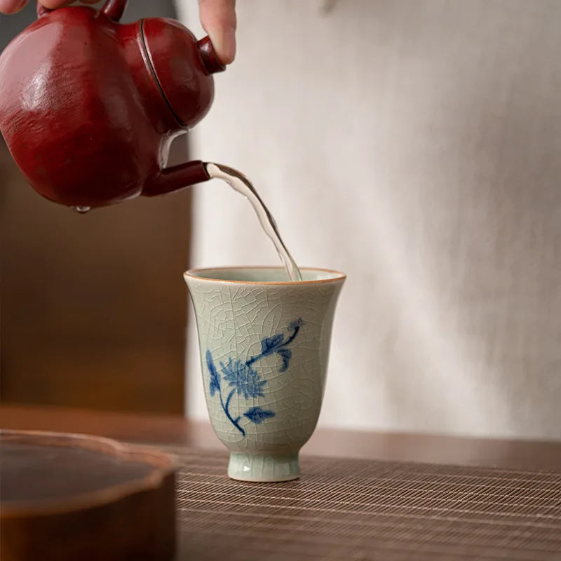 Théière rouge versant le thé dans une tasse céladon à décor d'orchidée
