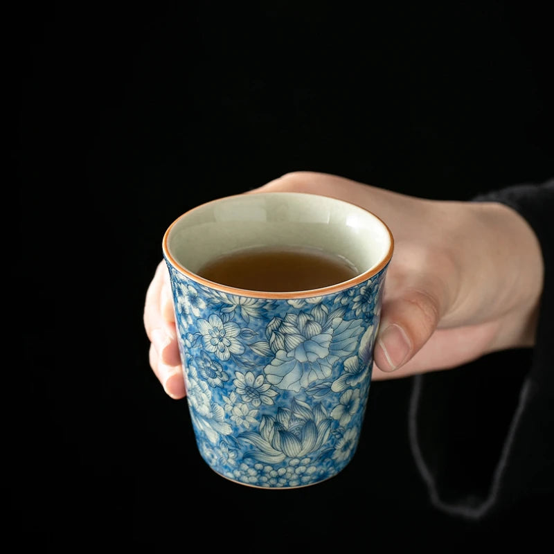 Tasse à thé bleu et blanc remplie, tenue en main sur fond noir