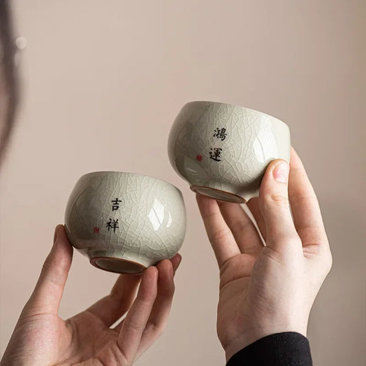 Deux tasses à thé céladon craquelé à vœux calligraphiés, tenues à deux mains