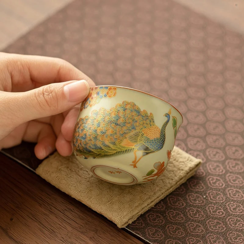 Tasse à thé à motif de paon inclinée sur un coussinet en lin
