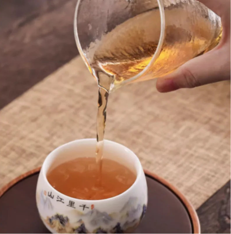 Pichet en verre versant le thé dans la tasse en porcelaine calligraphiée