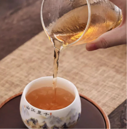 Pichet en verre versant le thé dans la tasse en porcelaine calligraphiée