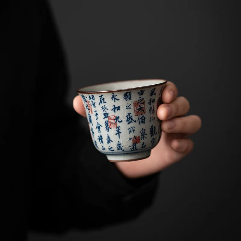 Tasse à thé à décor calligraphié tenue en main sur fond noir