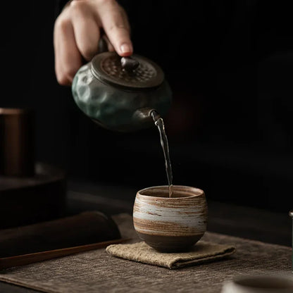 Théière en grès versant le thé dans la tasse posée sur un coussinet