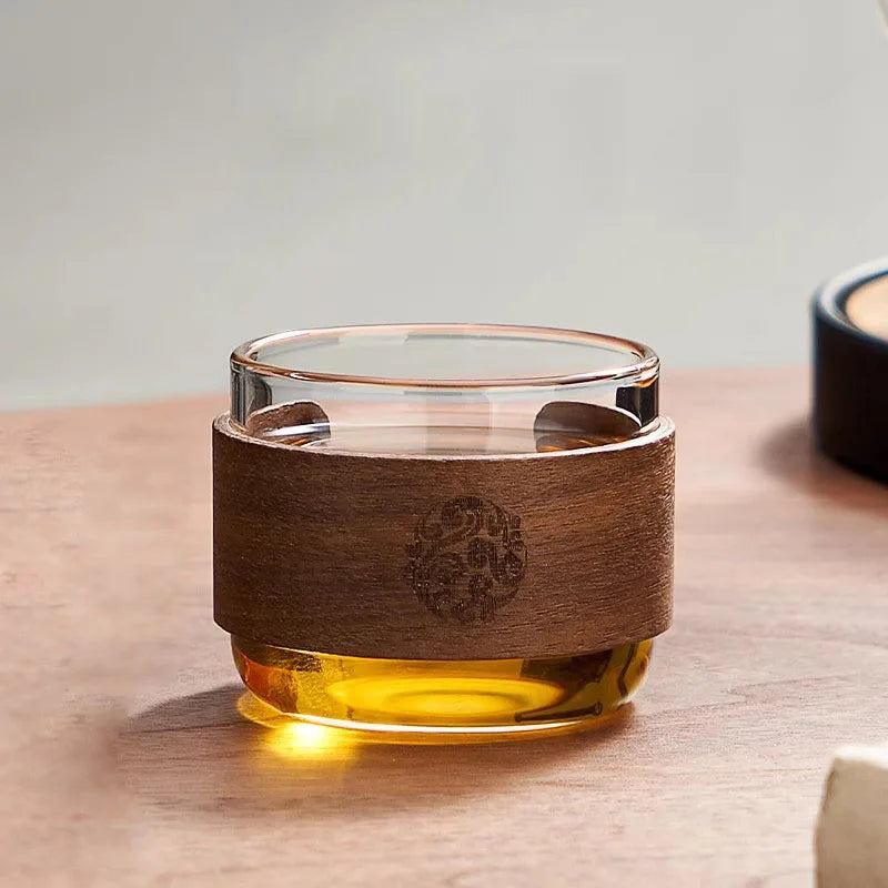 Tasse en verre à manchon en noyer remplie de thé, posée sur une table en bois