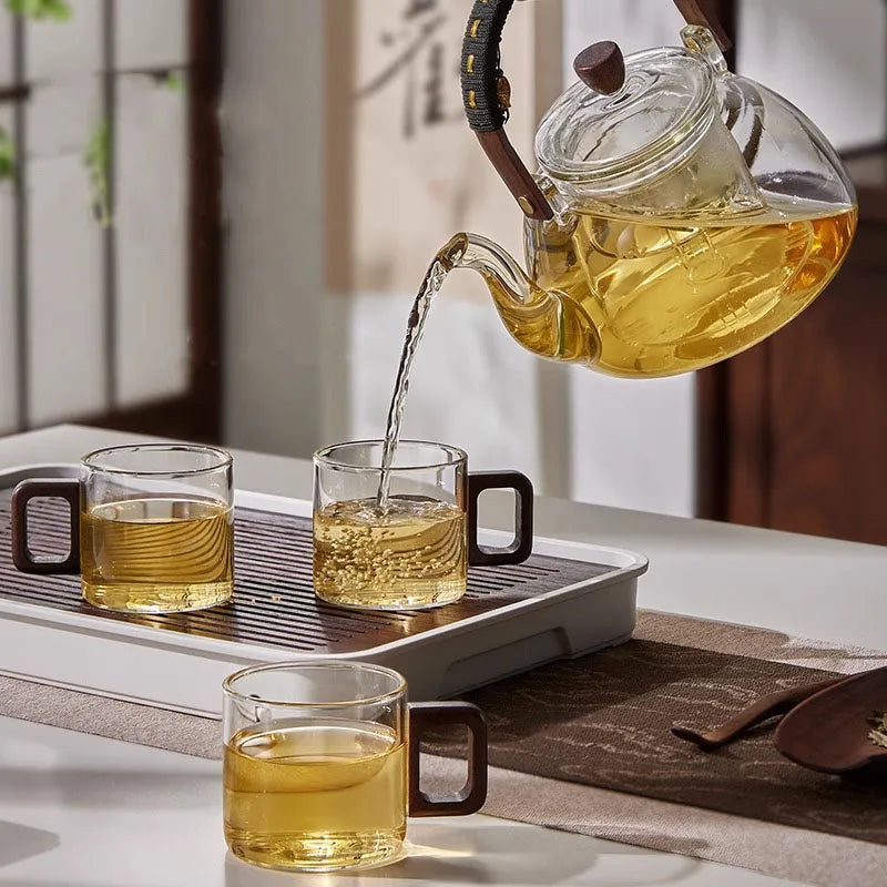 Théière en verre versant le thé dans les tasses à anse en bois du plateau