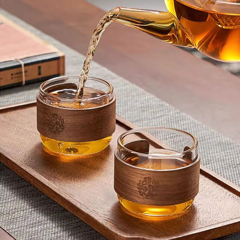 Théière en verre versant le thé dans deux tasses à anneau de bois