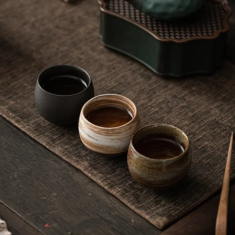 Trois tasses à thé en grès remplies, posées sur un chemin de table