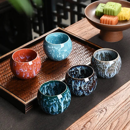 Cinq tasses à thé en céramique orange, turquoise et bleu nuit sur un plateau en bois