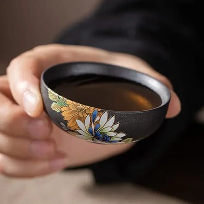 Tasse à thé noire remplie d'infusion, tenue entre le pouce et l'index
