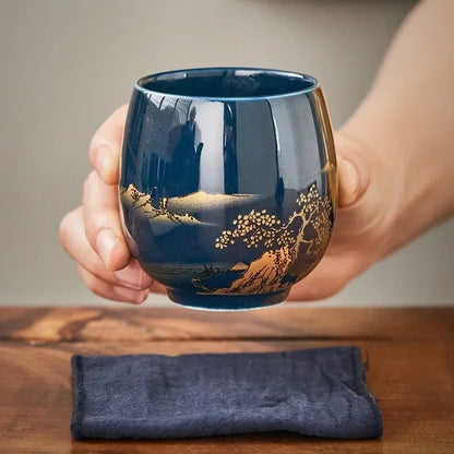Tasse à thé en céramique noire à décor doré tenue à deux mains
