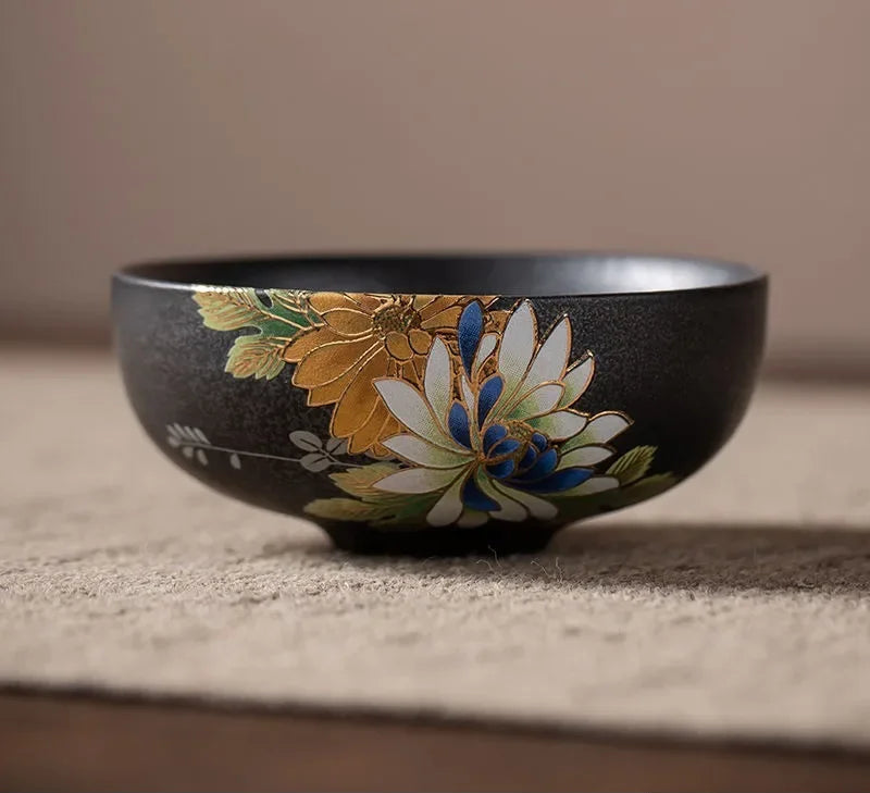 Tasse à thé en céramique noire à décor floral en relief, posée sur une natte