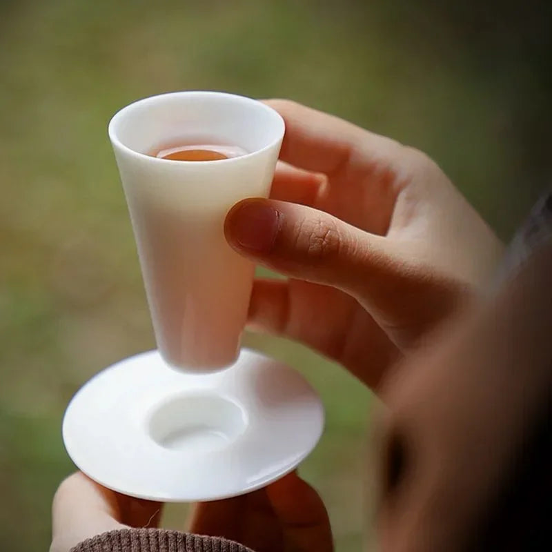 Tasse à thé sur sa soucoupe tenue en main devant un jardin