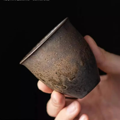 Tasse à thé aux reflets métalliques tenue inclinée sur fond noir