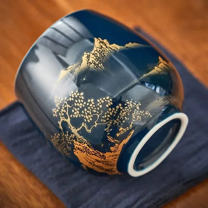 Tasse à thé renversée montrant son pied et son décor de paysage doré