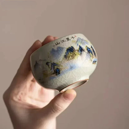 Tasse à thé à décor de paysage montagneux tenue inclinée dans la main