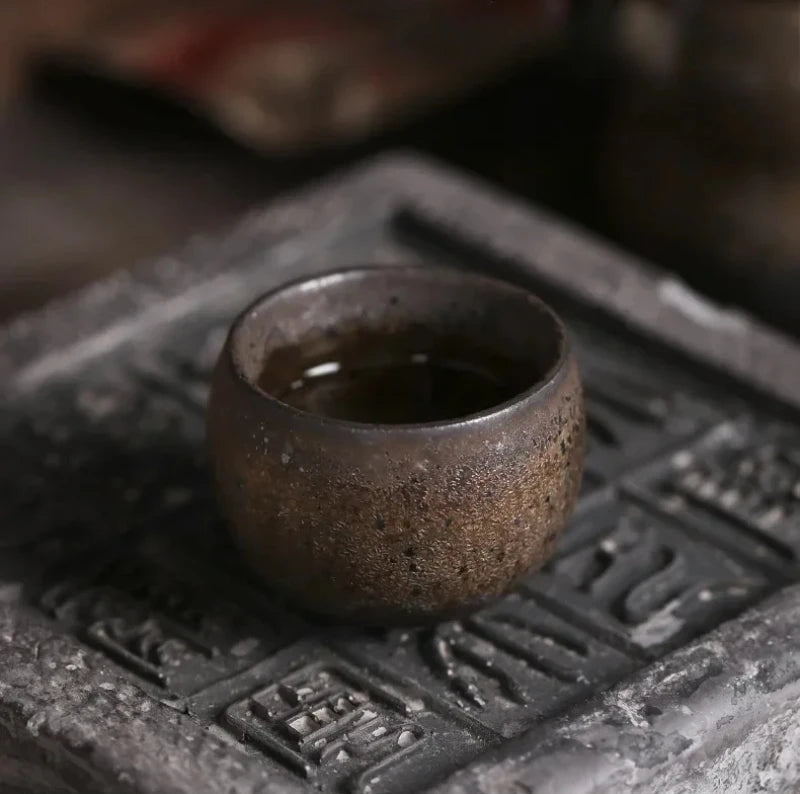 Tasse à thé en grès remplie d'infusion, posée sur un socle en pierre gravée