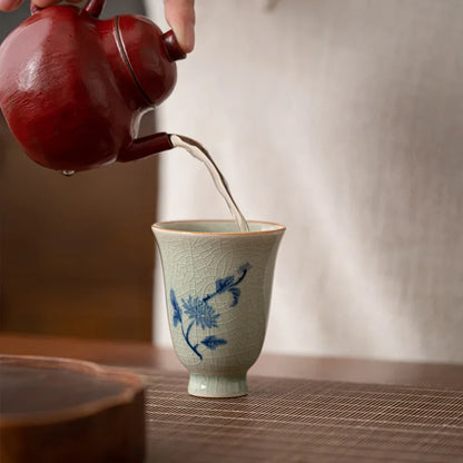 Théière rouge versant le thé dans une tasse céladon à décor d'orchidée