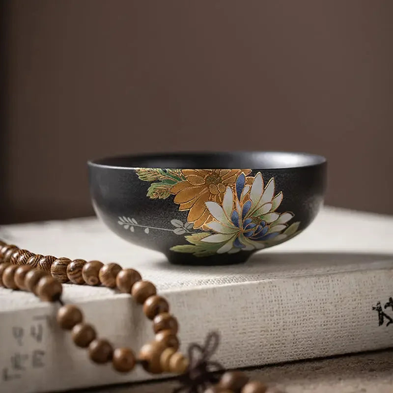 Tasse à thé noire à décor floral posée sur un livre, près d'un chapelet en bois