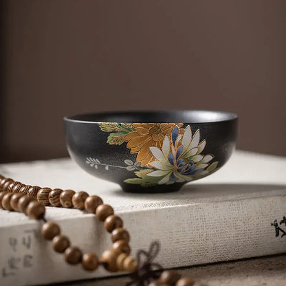Tasse à thé noire à décor floral posée sur un livre, près d'un chapelet en bois