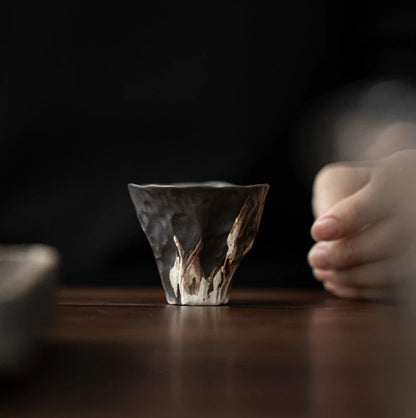 Tasse à thé wabi-sabi posée sur une table sombre, une main s'en approchant