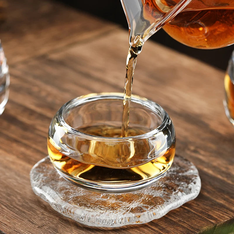 Versement du thé dans la tasse en verre posée sur un dessous en verre