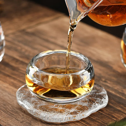 Versement du thé dans la tasse en verre posée sur un dessous en verre