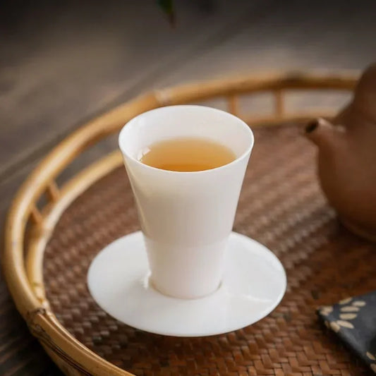 Tasse à thé en porcelaine blanche et sa soucoupe posées sur un plateau tressé
