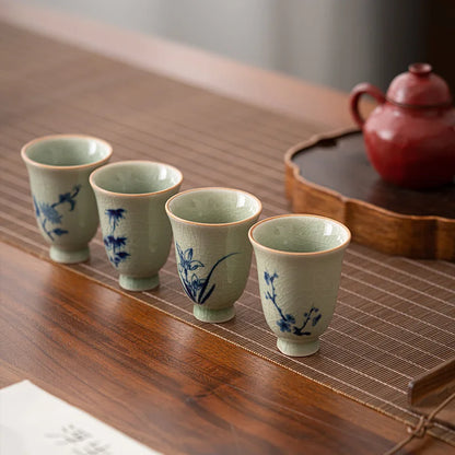 Lot de quatre tasses à thé céladon à décor floral bleu, alignées sur une table