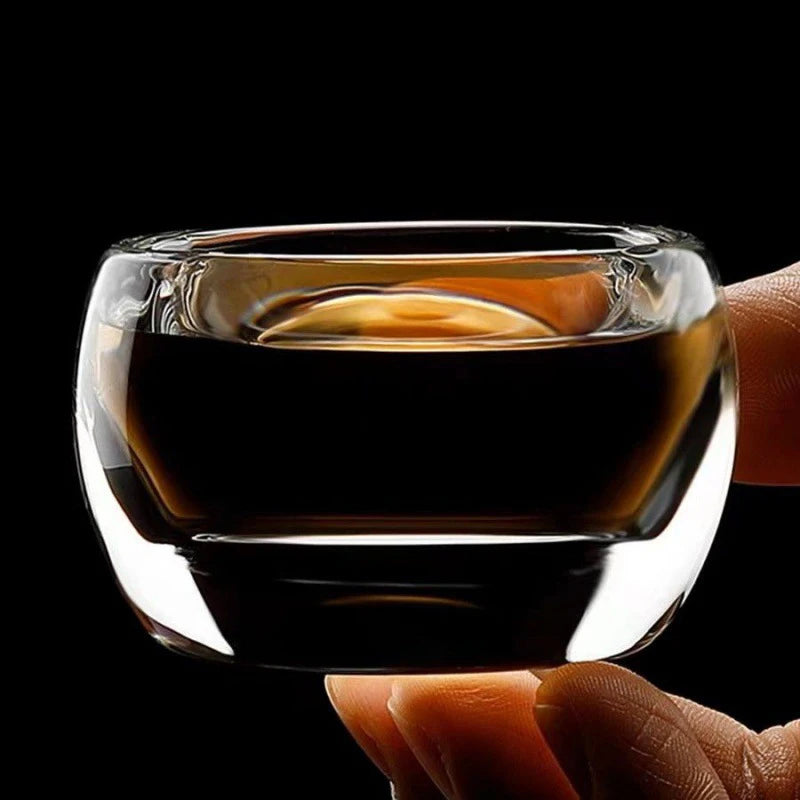 Tasse à thé en verre remplie de thé foncé, tenue entre les doigts