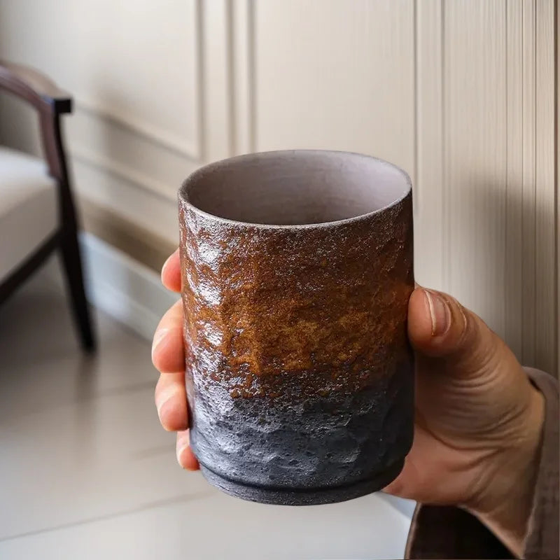 Grande tasse à thé en grès tenue en main devant une fenêtre