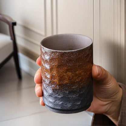 Grande tasse à thé en grès tenue en main devant une fenêtre