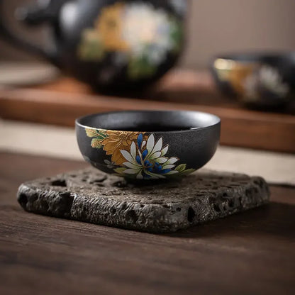 Tasse à thé noire à motif de lotus posée sur une pierre volcanique