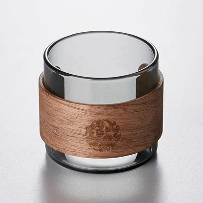Tasse à thé en verre fumé entourée de son anneau anti-brûlure en noyer