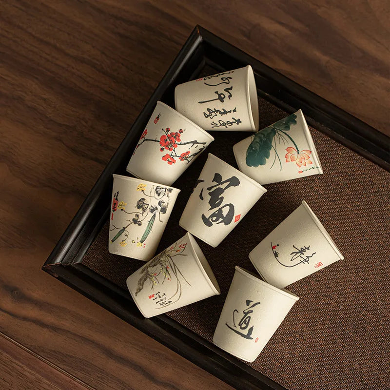 Huit tasses à thé en céramique aux décors à l'encre disposées sur un plateau