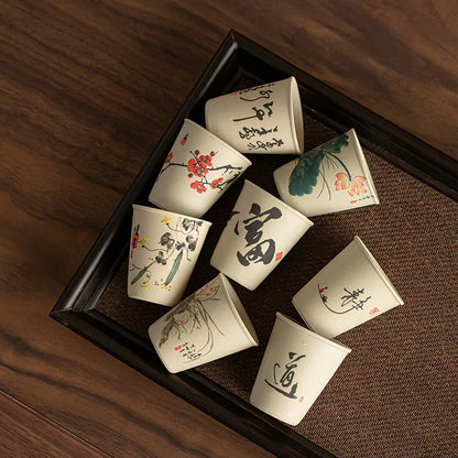 Huit tasses à thé en céramique aux décors à l'encre disposées sur un plateau
