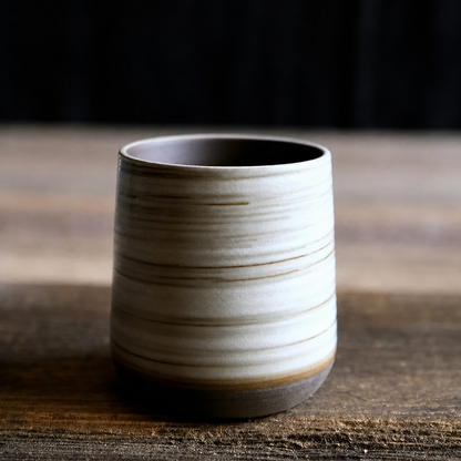 Tasse à thé en grès rayé coloris crème posée sur une table en bois brut