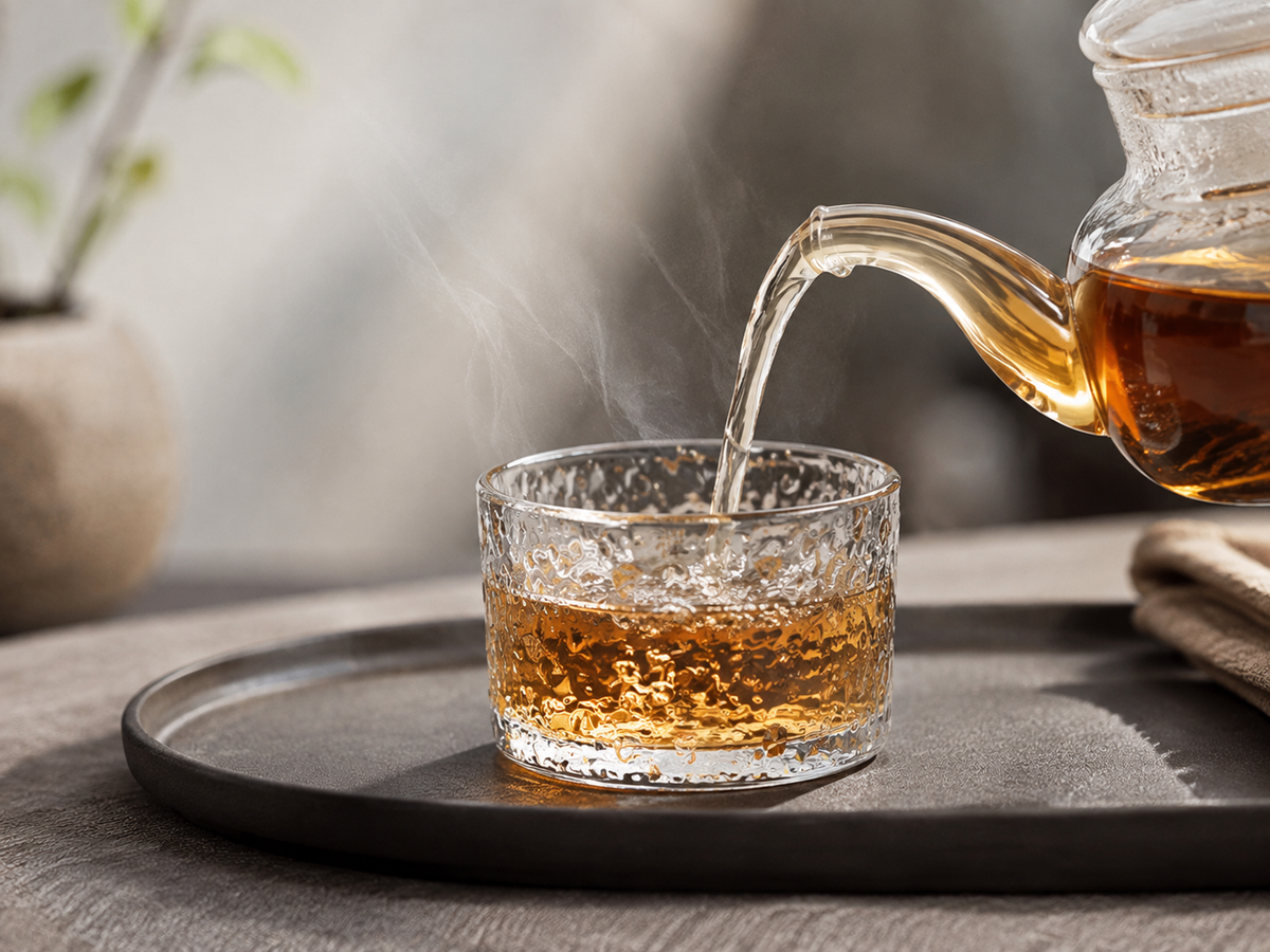 Théière en verre versant le thé dans la tasse en verre martelé